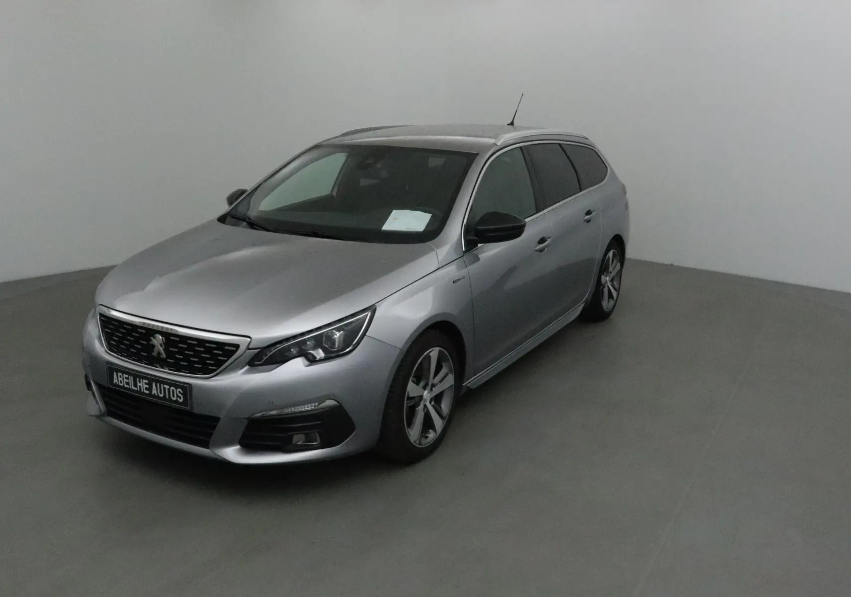 Peugeot 308 SW gris Artense vue 3/4 avant droit dans un studio, avec jantes alliage et calandre noire.
