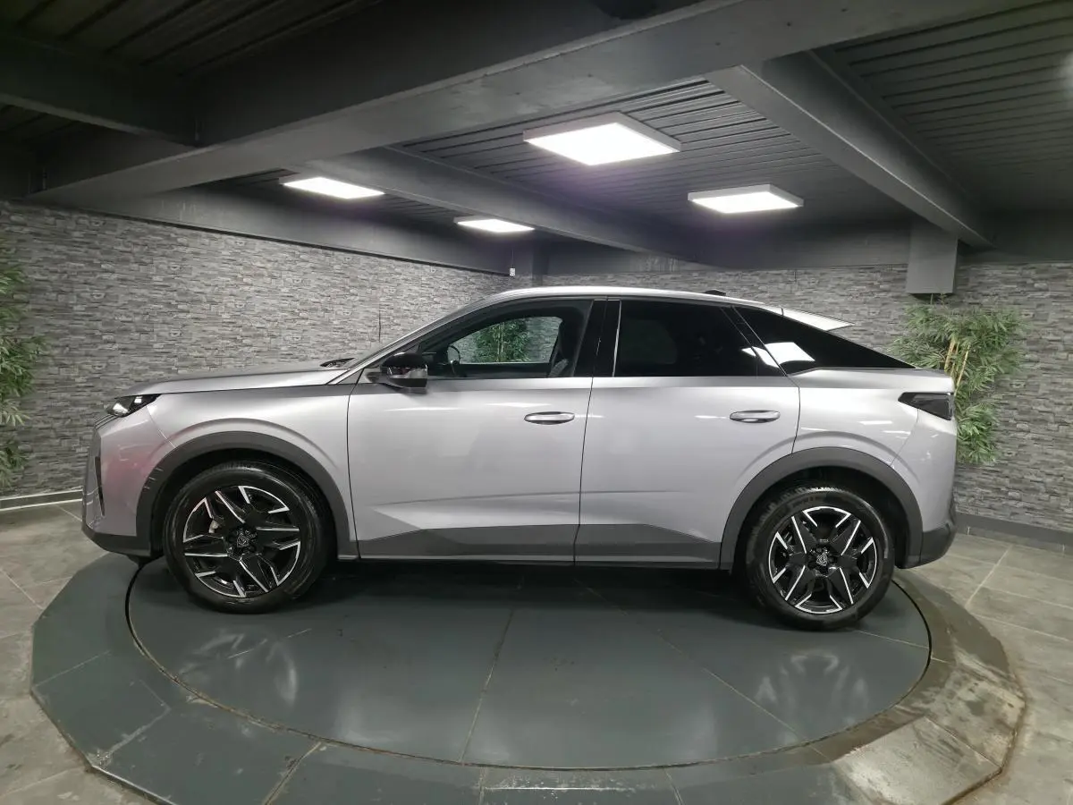 Vue latérale droite d'un Peugeot 3008 gris métallisé avec jantes alliage noires et toit noir en intérieur showroom.