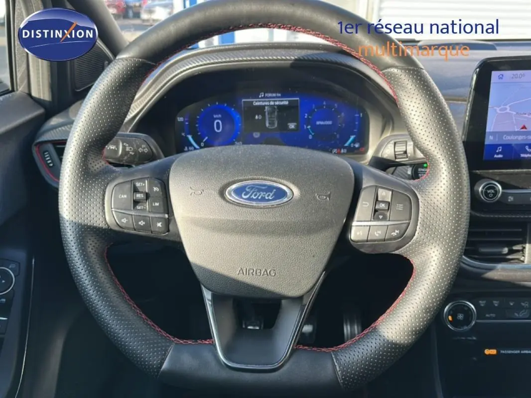 Vue centrée sur le volant perforé avec surpiqûres rouges du Ford Puma gris foncé, tableau de bord numérique et écran tactile visibles.