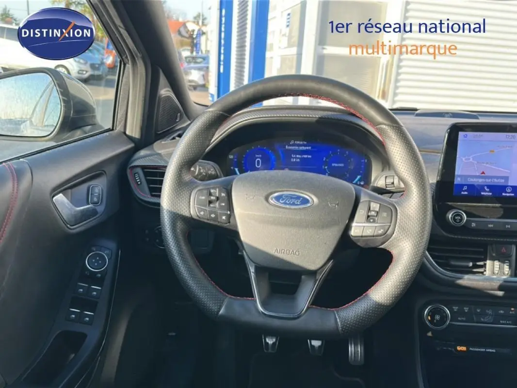 Vue intérieure centrée sur le volant perforé de la Ford Puma gris foncé avec tableau de bord numérique et écran tactile GPS.