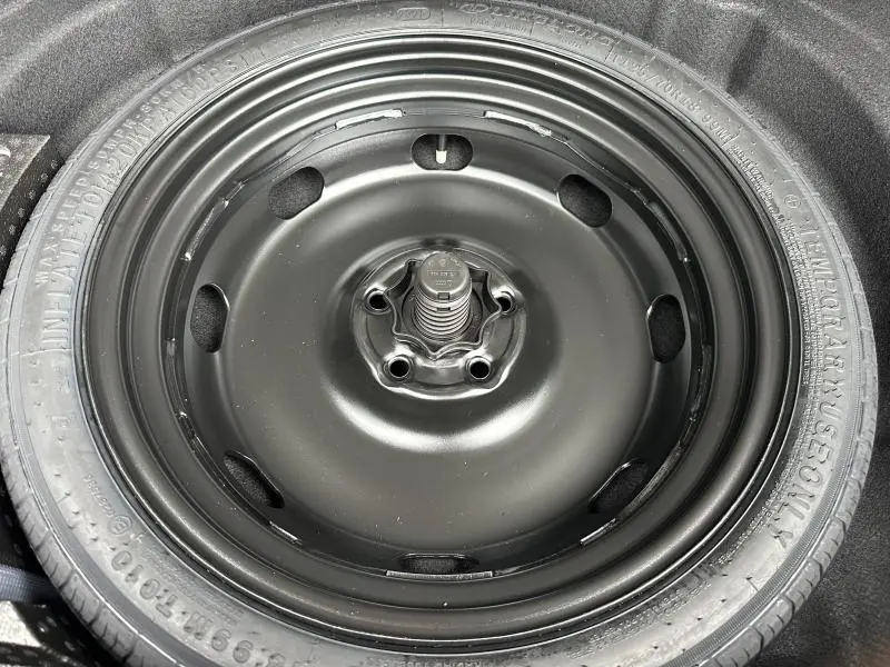 Gros plan sur la roue de secours noire montée sur un pneu temporaire dans le coffre d'une Volkswagen Golf gris 2026.