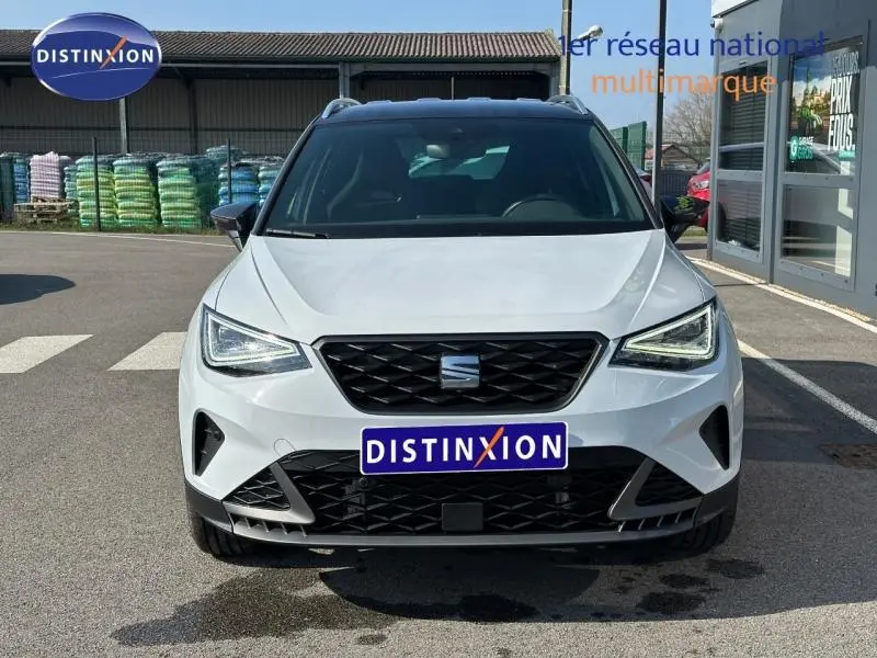 Vue frontale d'un SEAT Arona 2025 blanc Candy avec toit noir Minuit, calandre noire et feux LED allumés.