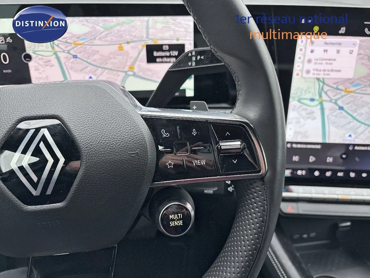 Gros plan sur le volant noir du Renault Austral 2023 avec commandes intégrées et écran tactile de navigation en arrière-plan.