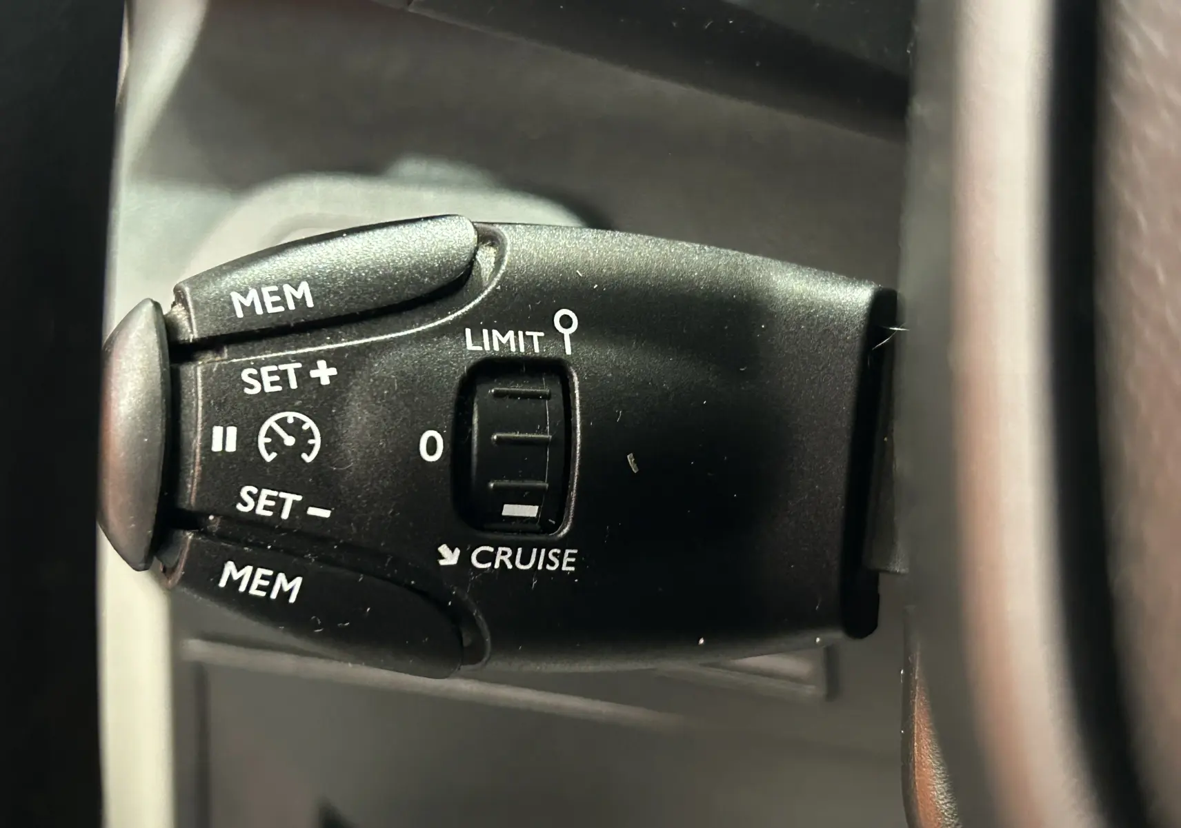 Gros plan sur la commande de régulateur de vitesse à gauche du volant dans un Peugeot Rifter gris sable 2019.