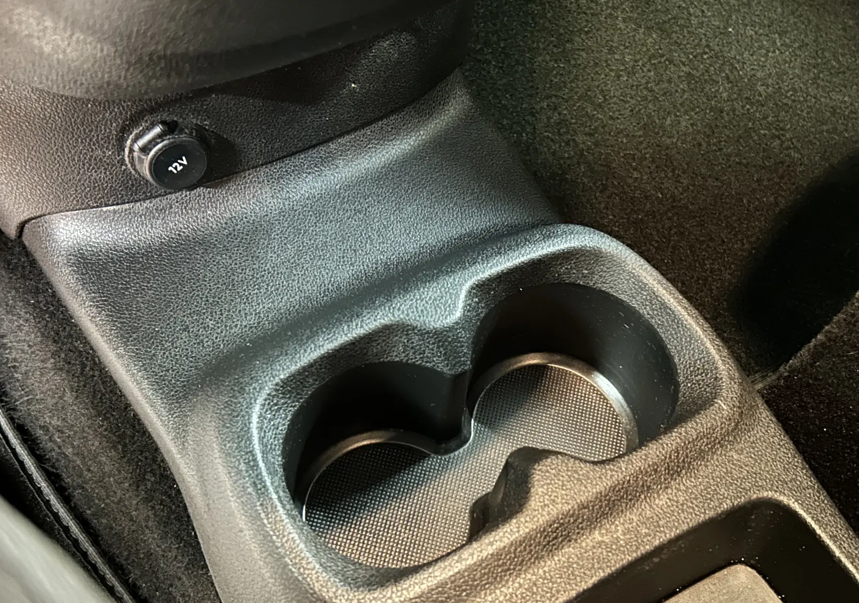 Gros plan sur le porte-gobelets central noir et la prise 12V dans l'habitacle du Peugeot Rifter 2019 gris sable.