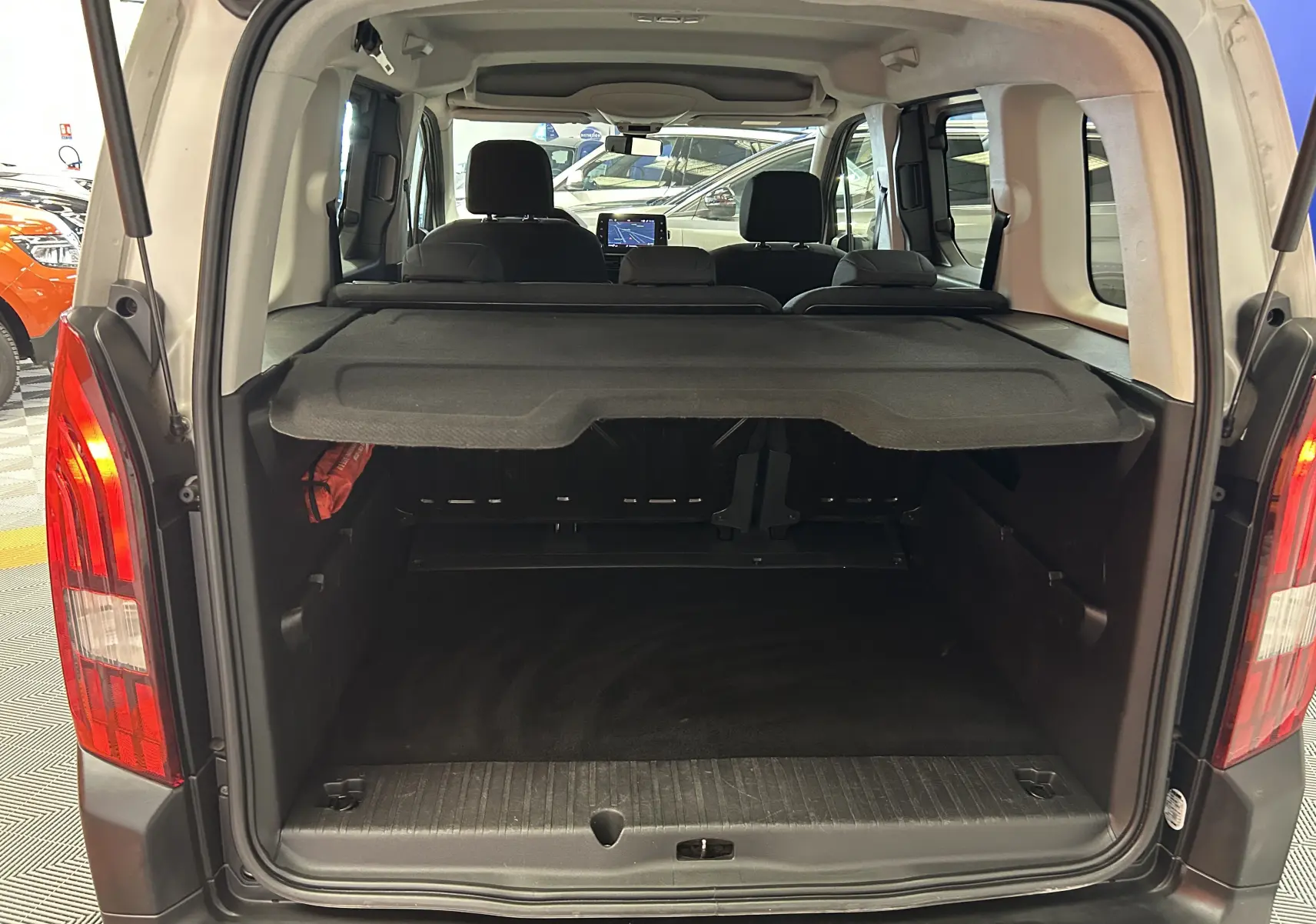 Coffre ouvert vu de l'arrière d'un Peugeot Rifter gris sable 2019 avec cache-bagages et sièges arrière visibles.