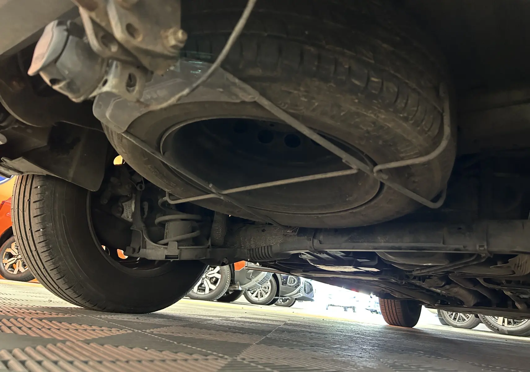 Vue en contre-plongée sous le PEUGEOT RIFTER gris sable, montrant la roue de secours et le train arrière.