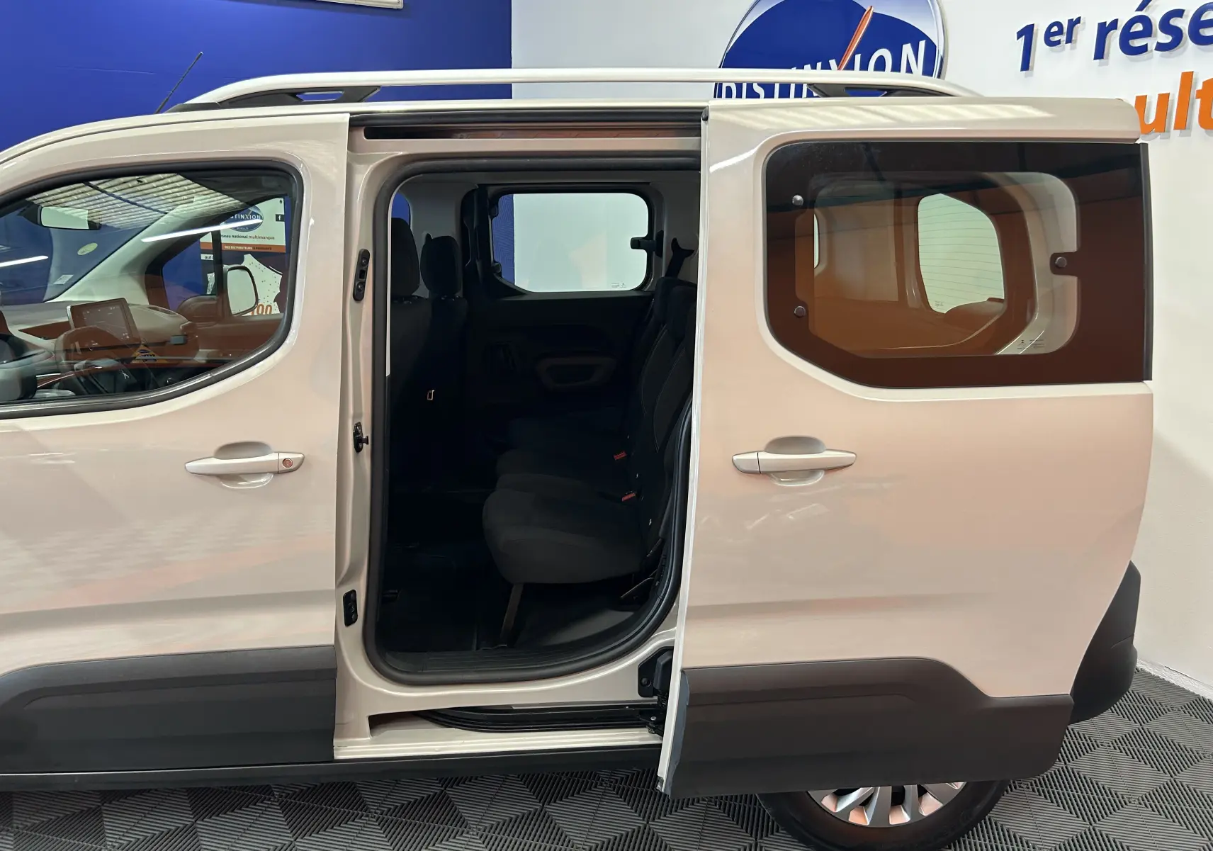 Vue latérale droite du Peugeot Rifter gris sable 2019 avec porte coulissante ouverte dévoilant l'intérieur à trois sièges.