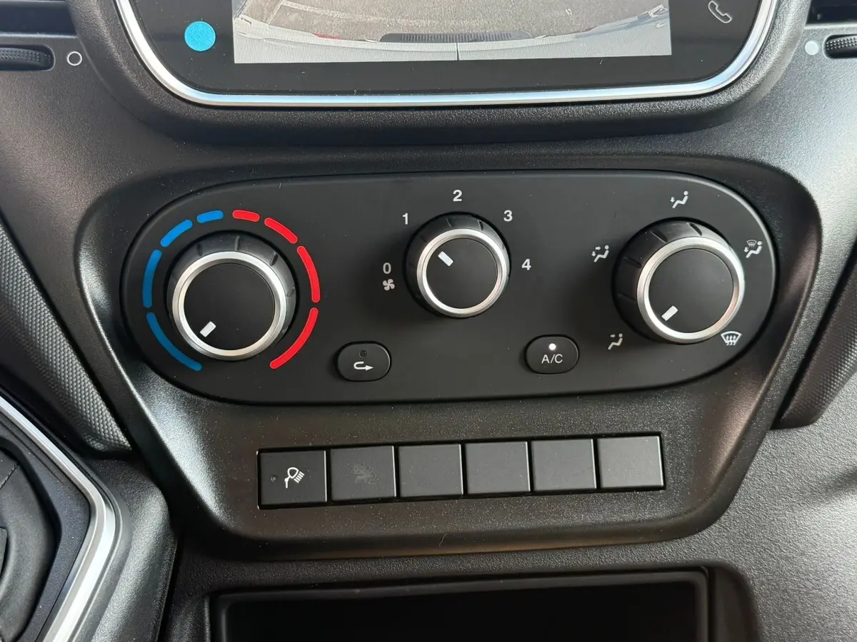Vue rapprochée du tableau de commande de climatisation noir du Iveco Daily blanc, avec trois boutons rotatifs et écran supérieur partiel.