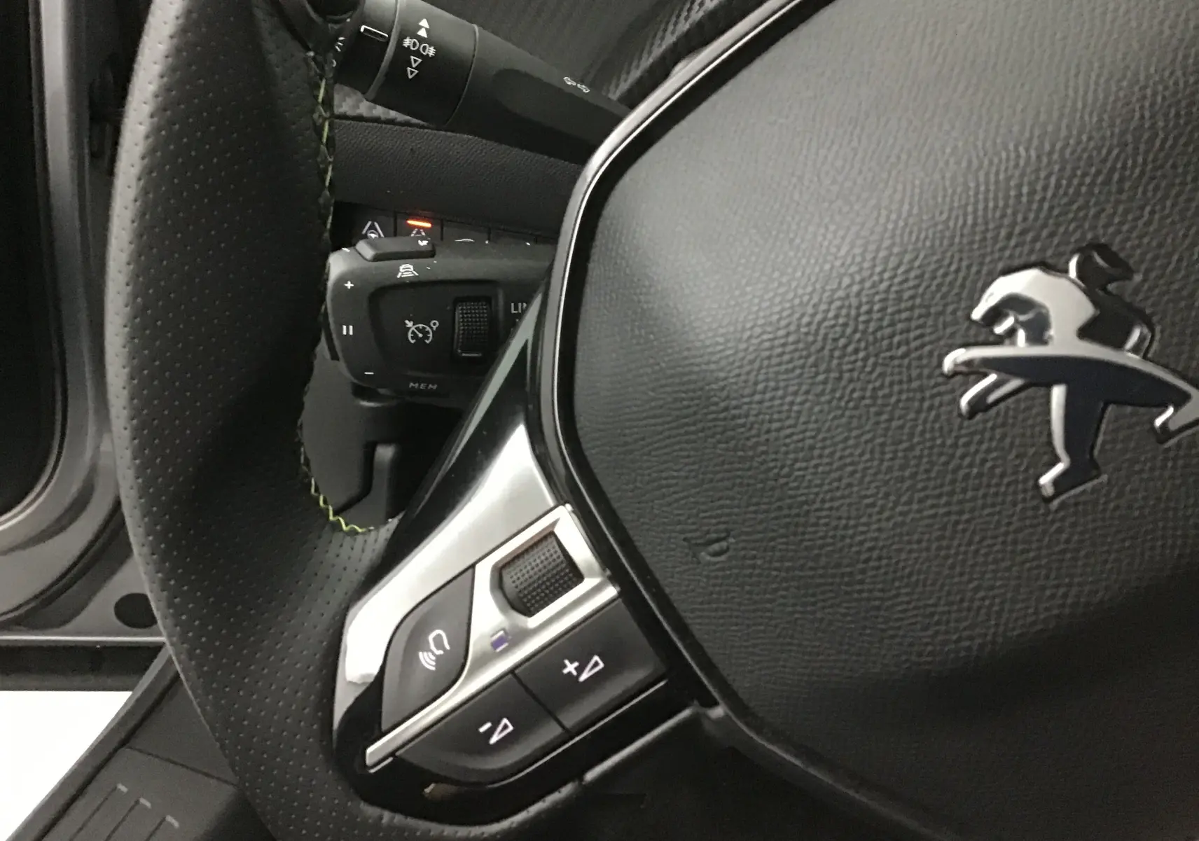 Gros plan sur le volant cuir noir perforé du Peugeot 2008 électrique 2022 avec commandes intégrées et logo lion argenté.