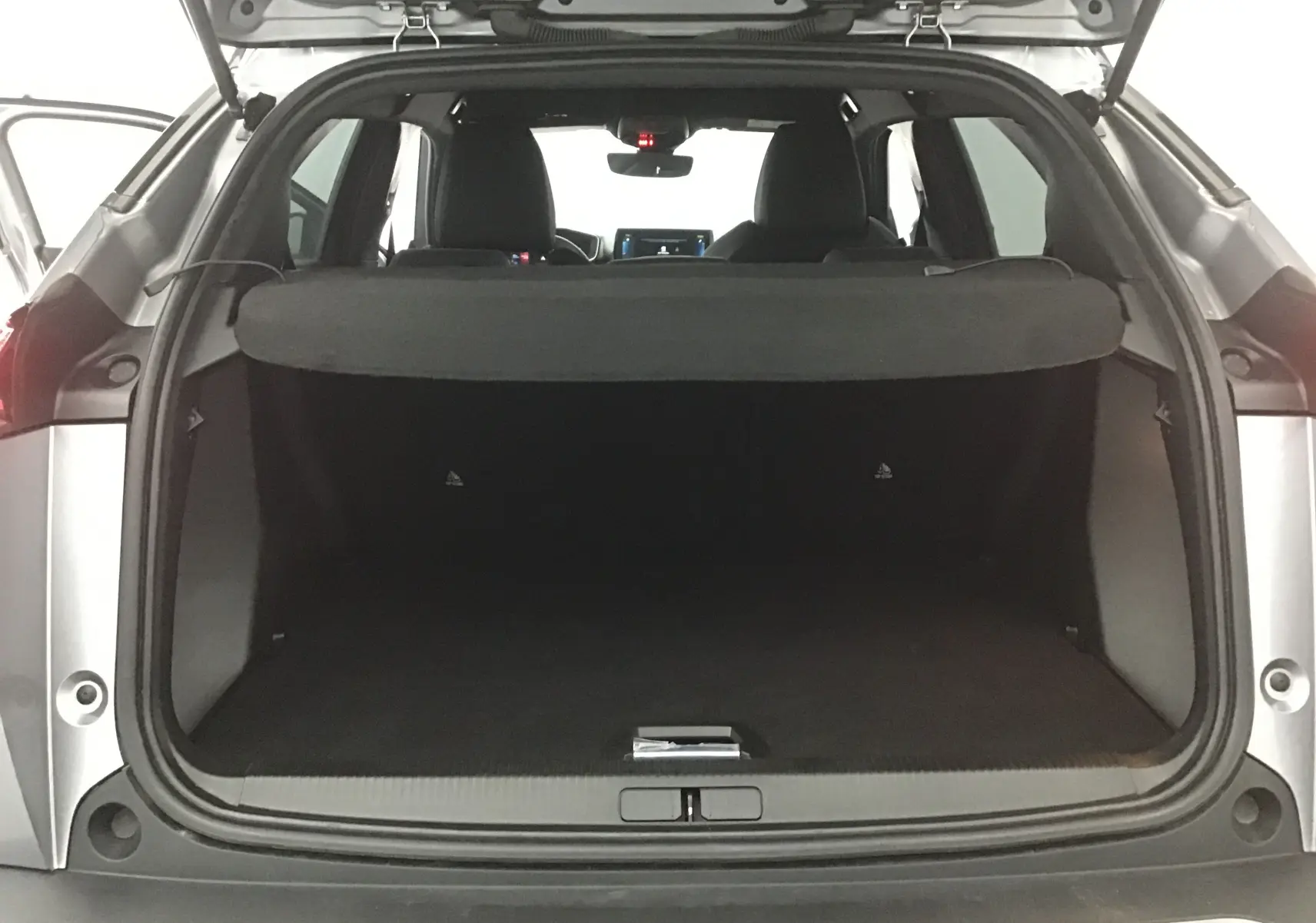 Coffre ouvert vu de l'arrière d'un Peugeot 2008 électrique gris Artense avec intérieur noir et tablette de séparation.