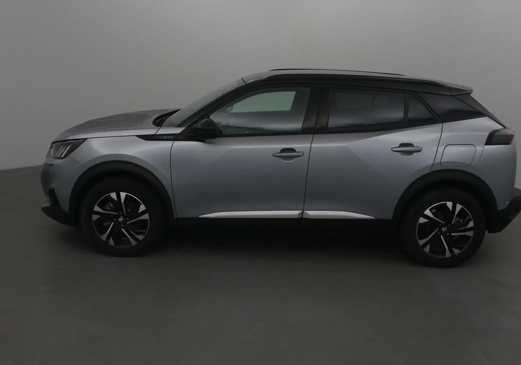 Profil côté gauche du Peugeot 2008 électrique 2022 en gris Artense avec toit noir et jantes noires distinctives.
