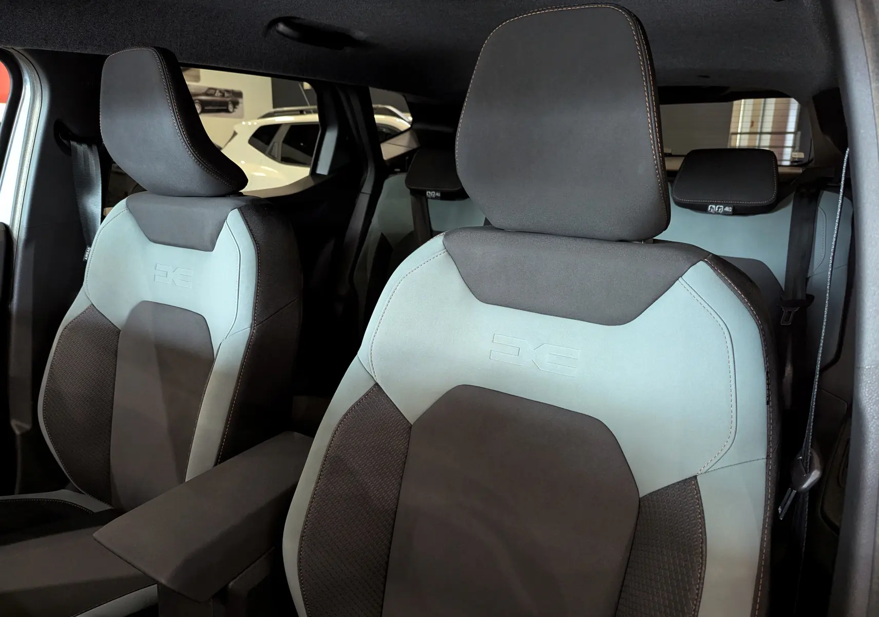 Gros plan sur les sièges avant bi-ton gris clair et foncé du Dacia Duster Mild Hybrid 2025, intérieur moderne et épuré.