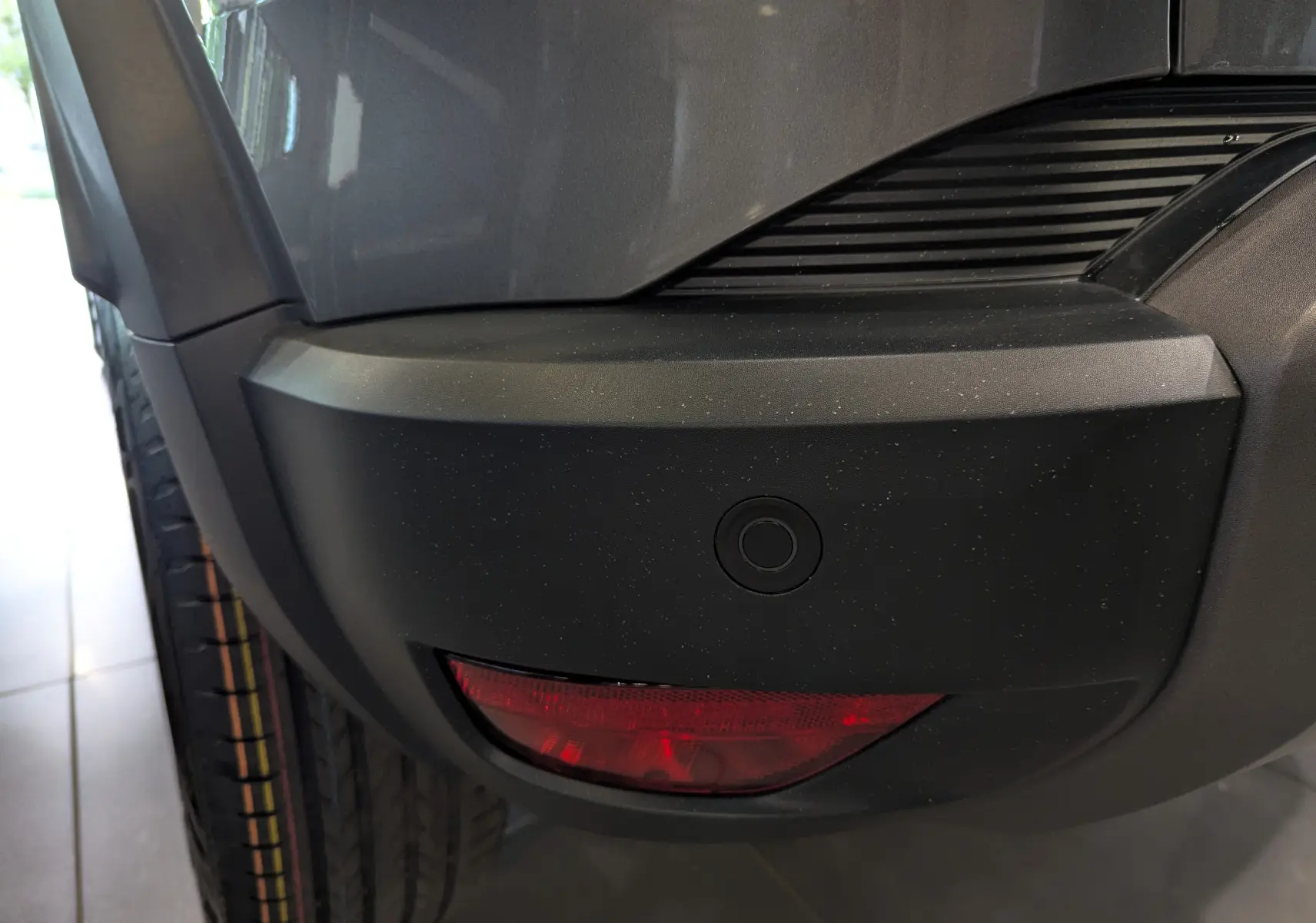 Gros plan sur le pare-chocs arrière gris schiste du Dacia Duster 2025 avec feu antibrouillard et capteur de recul.