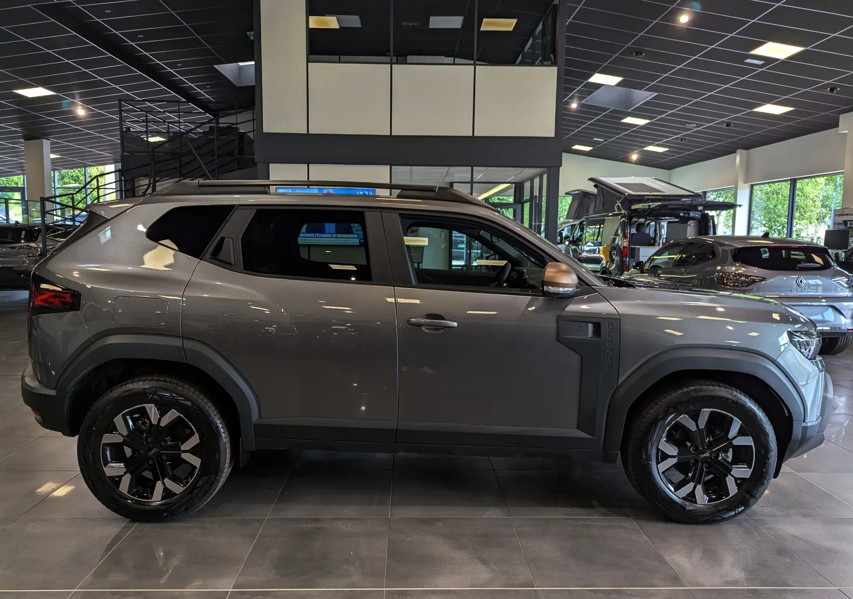 Profil côté droit du Dacia Duster 2025 gris schiste Mild Hybrid 130 CH 4x2 EXTRÊME en showroom avec jantes noires et grises.