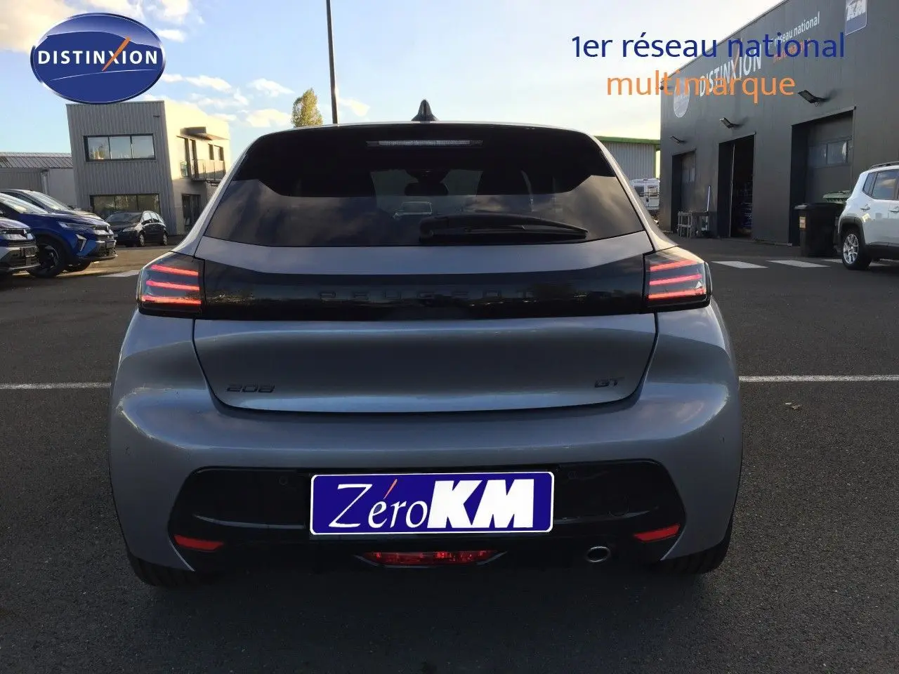 Vue arrière d'une Peugeot 208 GT gris Artense métal avec feux arrière LED allumés sur un parking extérieur.