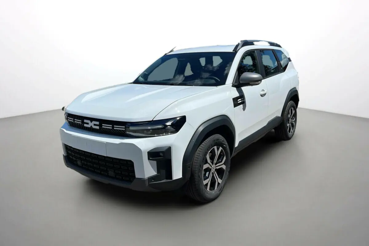 SUV Dacia Bigster blanc glacier en vue 3/4 avant droit avec barres de toit et jantes alu 17 pouces.