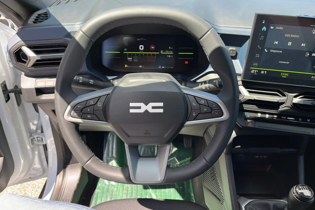 Vue intérieure centrée sur le volant cuir et le tableau de bord numérique du Dacia Bigster blanc glacier 2025.