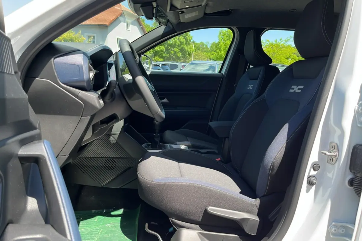 Vue intérieure côté gauche du DACIA BIGSTER blanc glacier 2025, sièges avant avec logo et tableau de bord moderne.