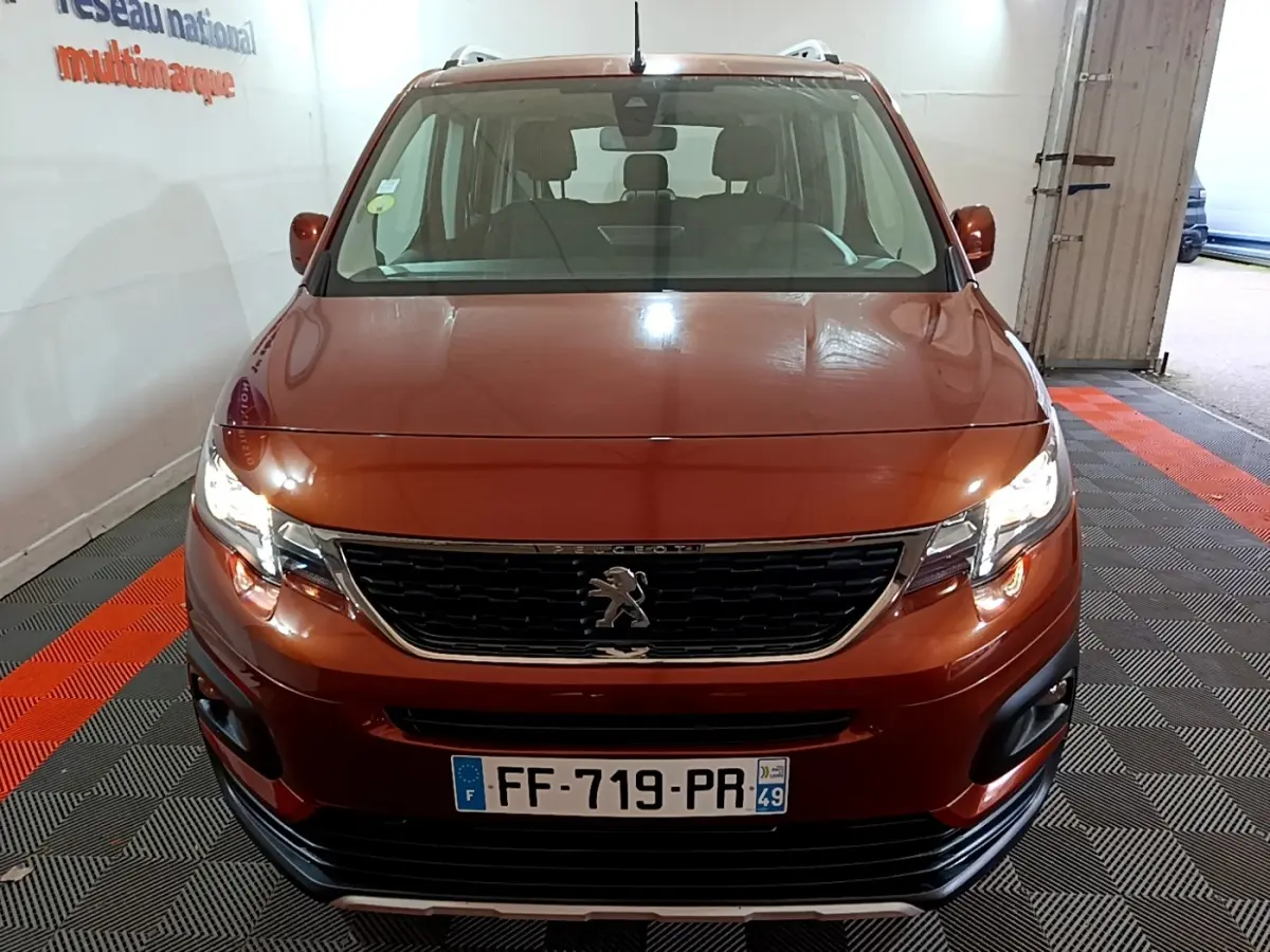 Vue avant d'un Peugeot Rifter BlueHDi 100 Allure marron avec phares allumés et calandre noire chromée.