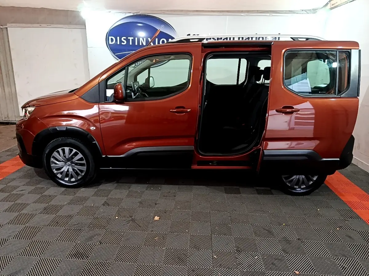 Profil côté gauche d'un Peugeot Rifter marron 2019 avec porte coulissante arrière ouverte en intérieur showroom.