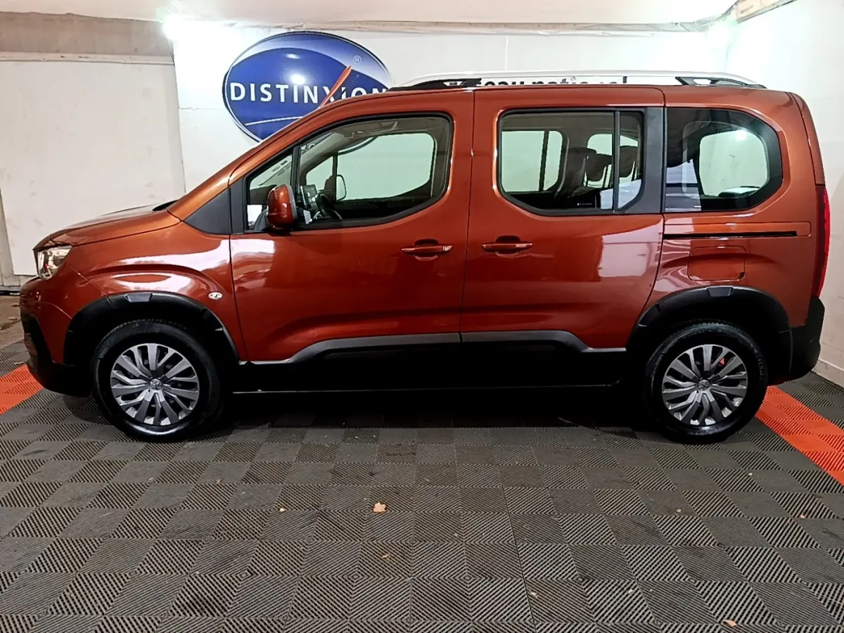 Profil côté gauche d'un Peugeot Rifter marron 2019 avec barres de toit chromées et jantes alliage en intérieur showroom.