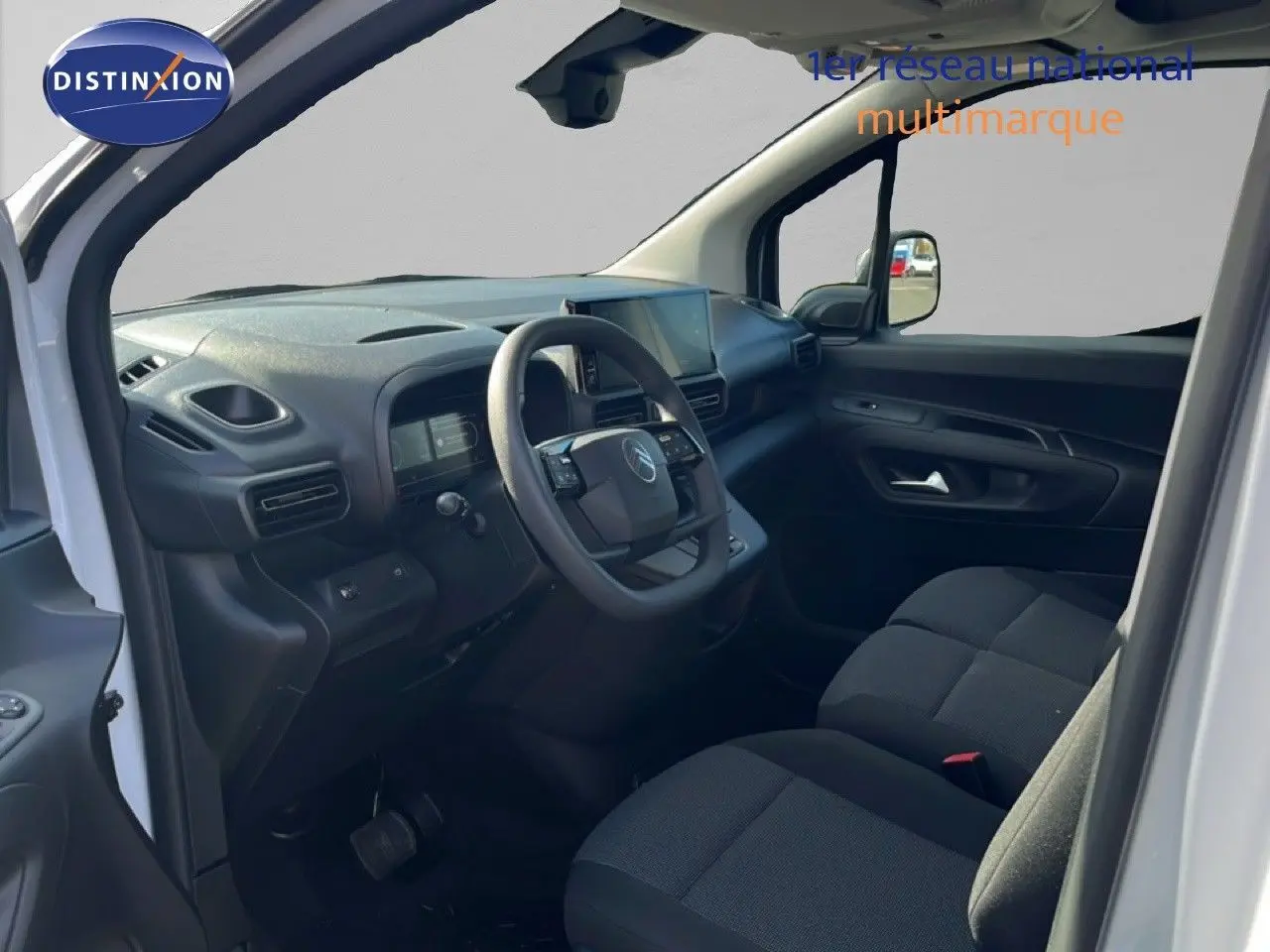 Vue intérieure côté conducteur du Citroën Berlingo blanc Icy 2025, tableau de bord et sièges noirs en tissu visibles.