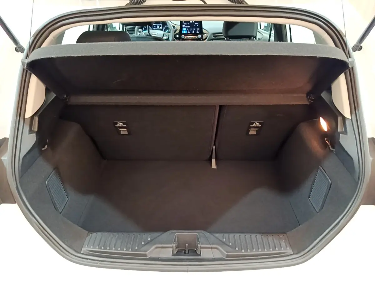 Coffre ouvert vu de l'arrière d'une Ford Fiesta blanche 2022, intérieur noir et tablette de coffre relevée.