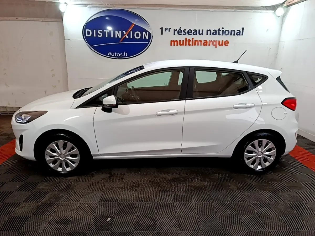 Vue de profil côté gauche d'une Ford Fiesta blanche 2022 dans un showroom avec sol noir et rouge.