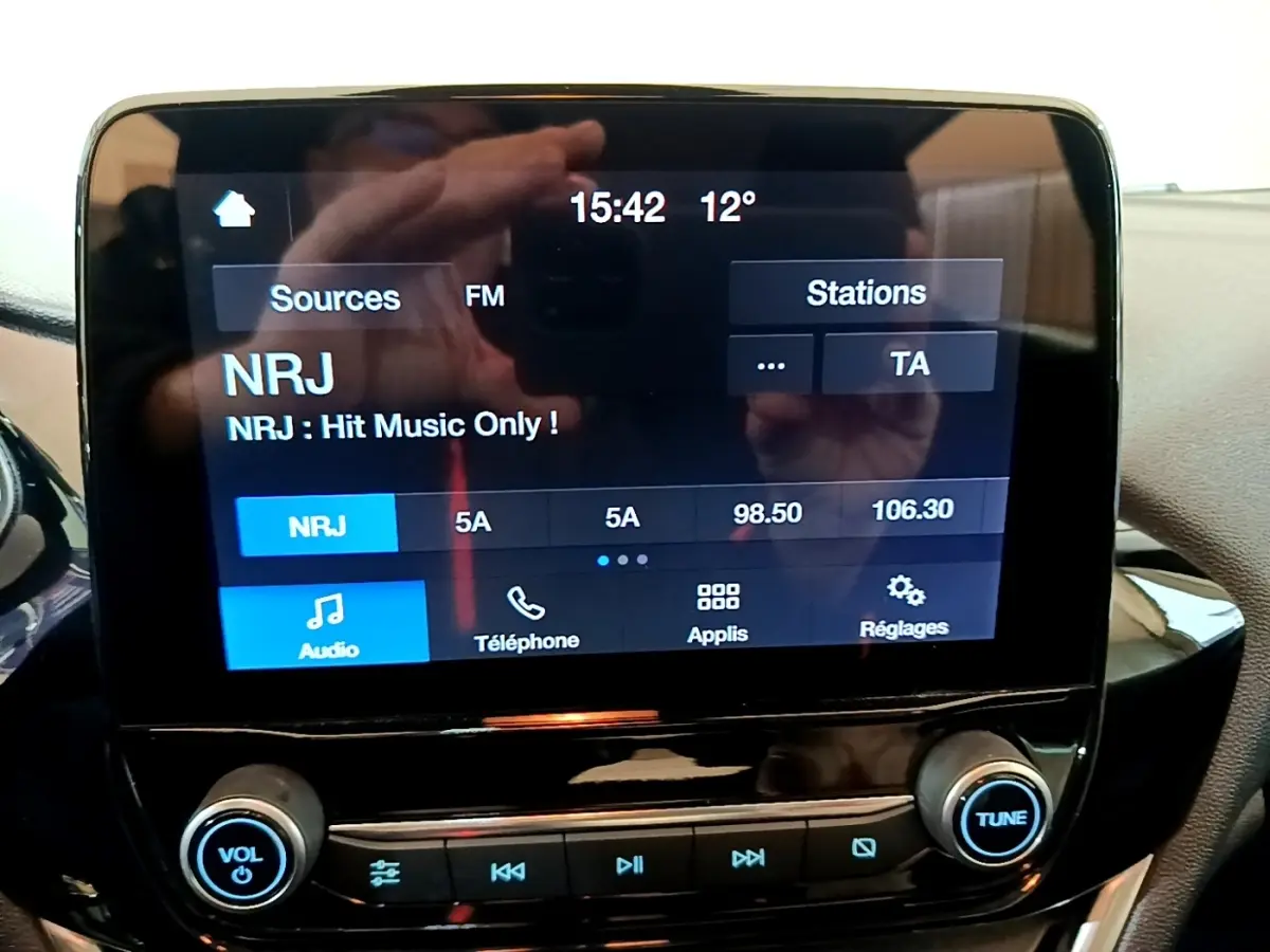 Écran tactile central de la Ford Fiesta blanche 2022 affichant la radio NRJ, vue intérieure frontale rapprochée.