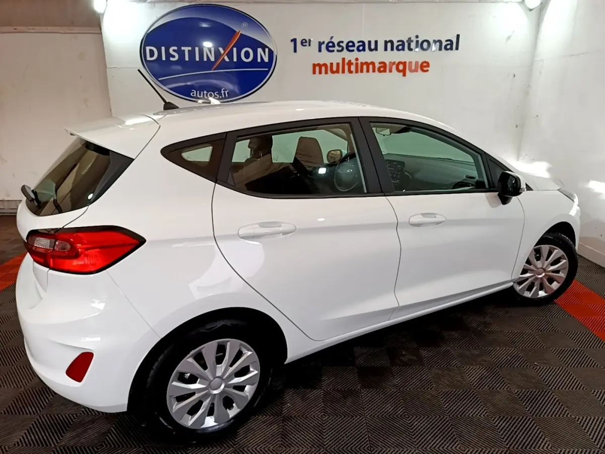 Ford Fiesta blanche vue de profil droit en intérieur, avec jantes acier et vitres teintées arrière.