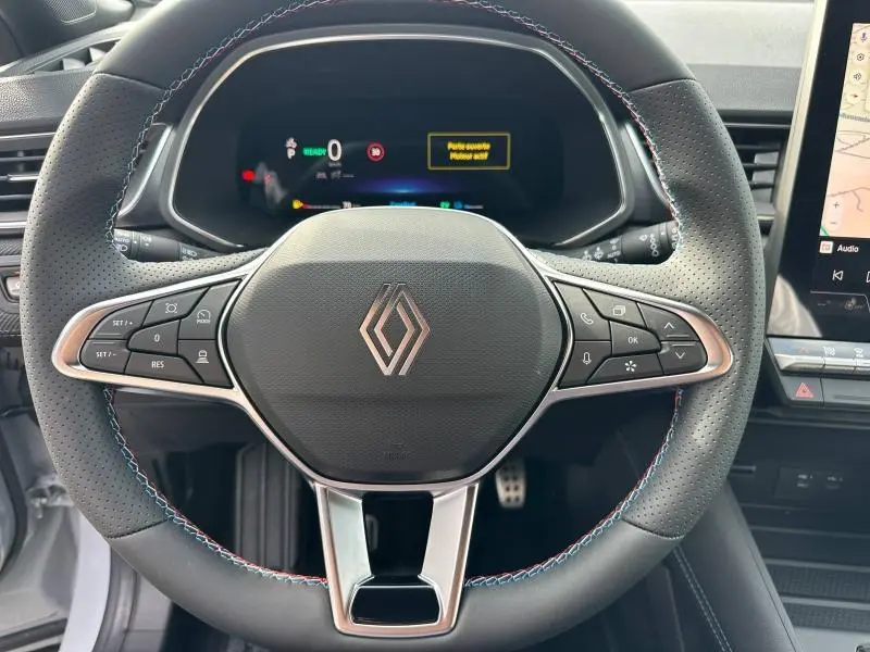 Vue rapprochée du volant perforé du Renault Captur 2026 avec coutures tricolores et tableau de bord numérique allumé.