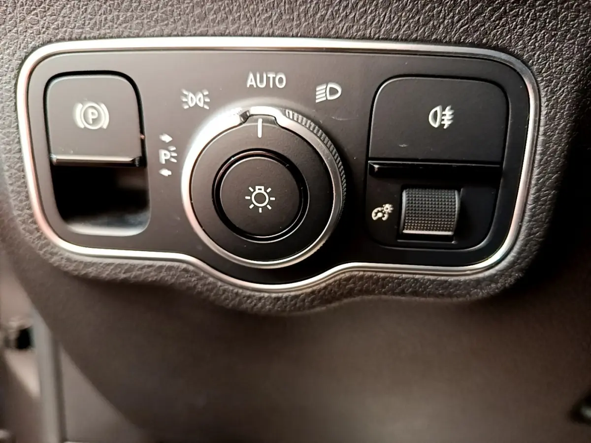 Gros plan sur le bouton de commande des phares et du frein à main électrique dans l'habitacle noir du Mercedes GLB 200 d.