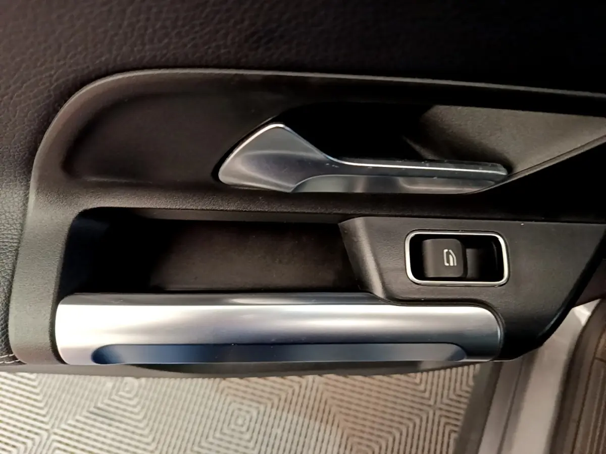 Gros plan sur la poignée intérieure et commande de vitre de la porte avant droite du Mercedes GLB 200 d gris foncé.