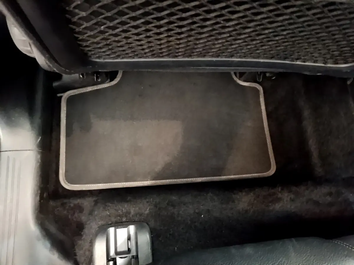 Vue rapprochée du tapis de sol gris foncé au sol, avec filet de rangement sous le siège arrière d’un Mercedes GLB 200 d.
