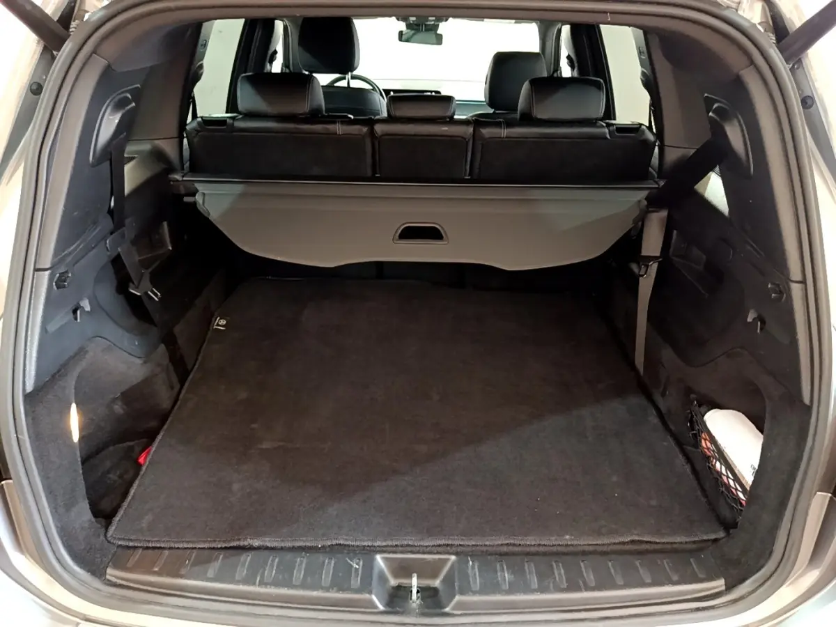 Coffre ouvert vu de l'arrière d'un Mercedes GLB 200 d Business Line gris foncé avec cache-bagages déployé.