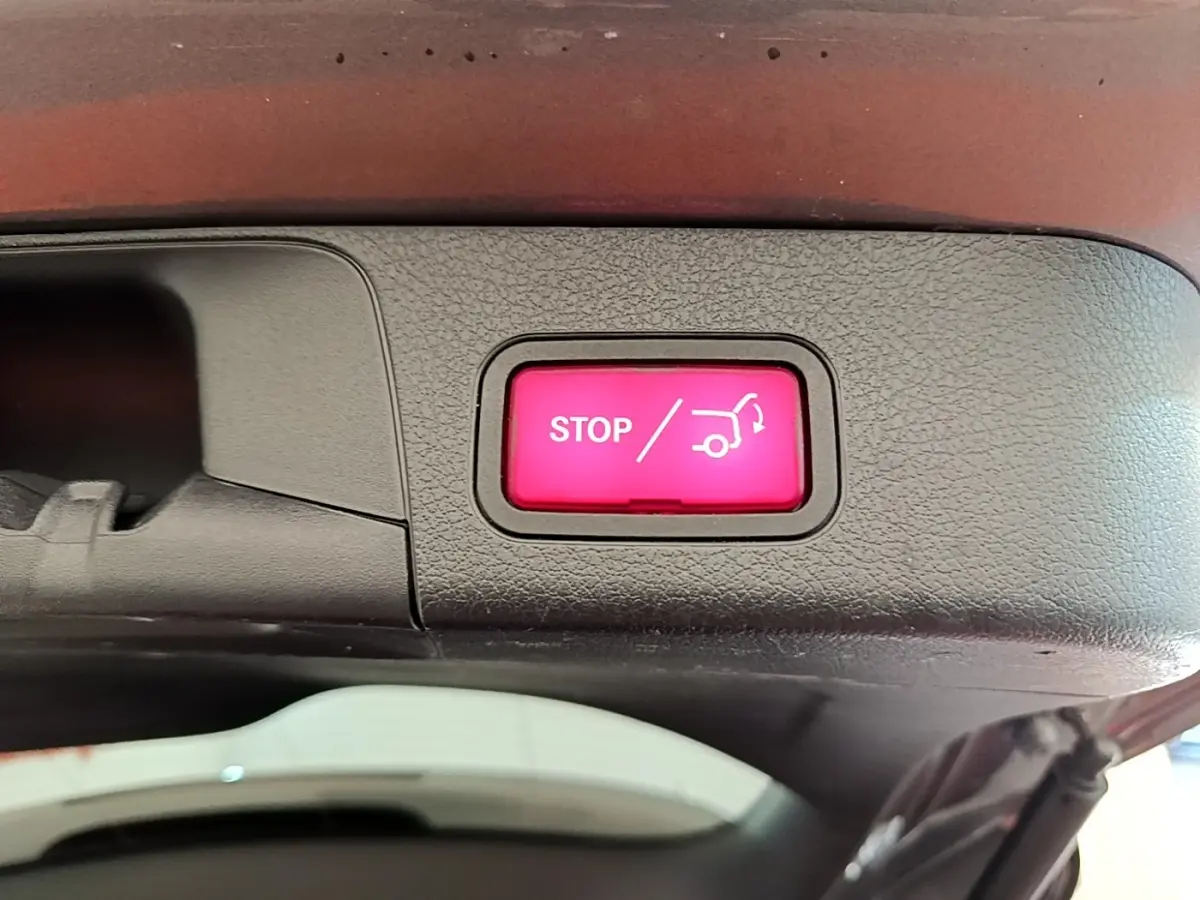 Bouton rouge STOP pour fermeture électrique du coffre, visible sur la partie intérieure du hayon d’un Mercedes GLB gris foncé.