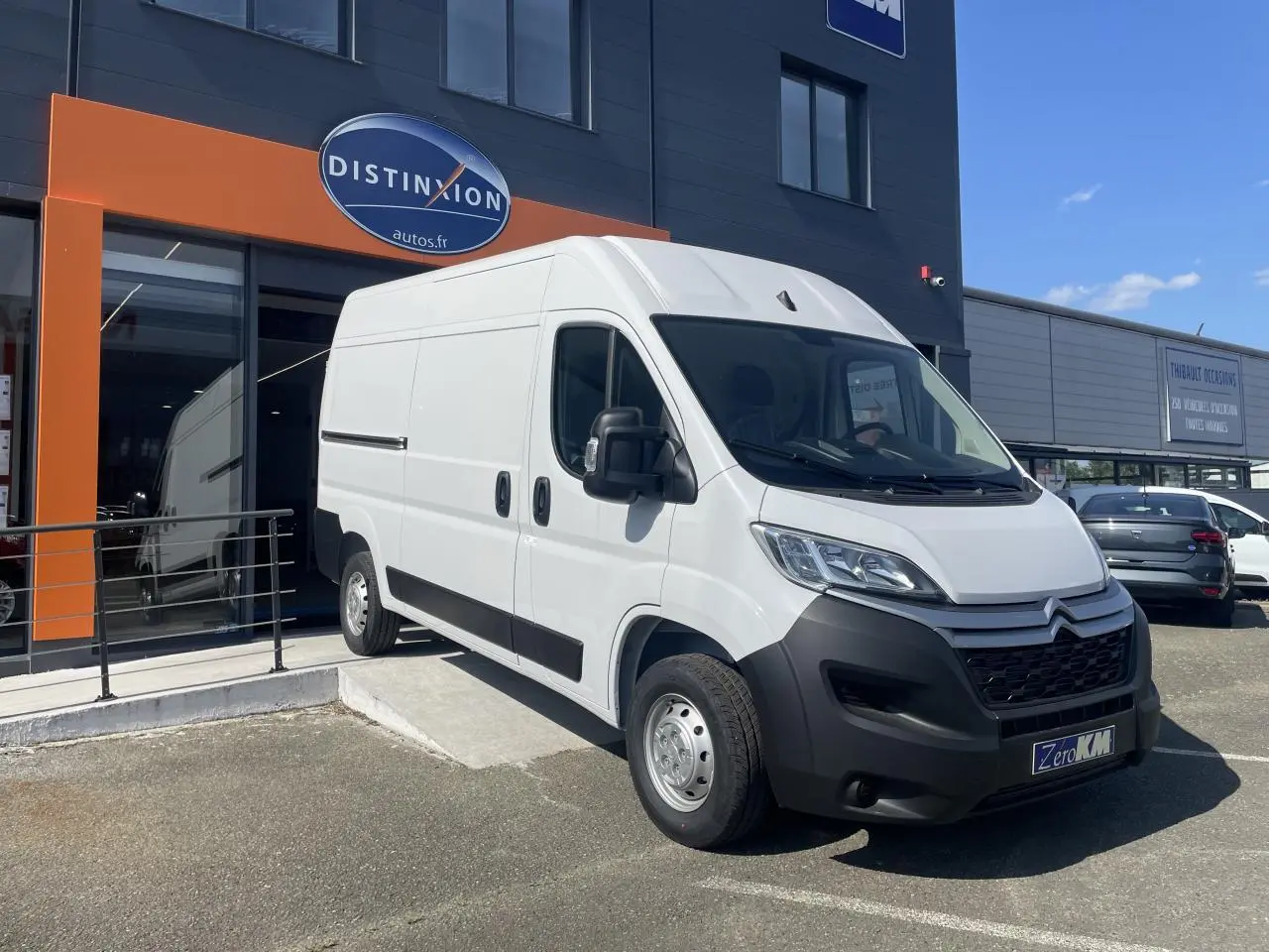 Vue 3/4 avant droite d’un Citroën Jumper blanc 2023 garé devant un bâtiment commercial avec calandre noire.