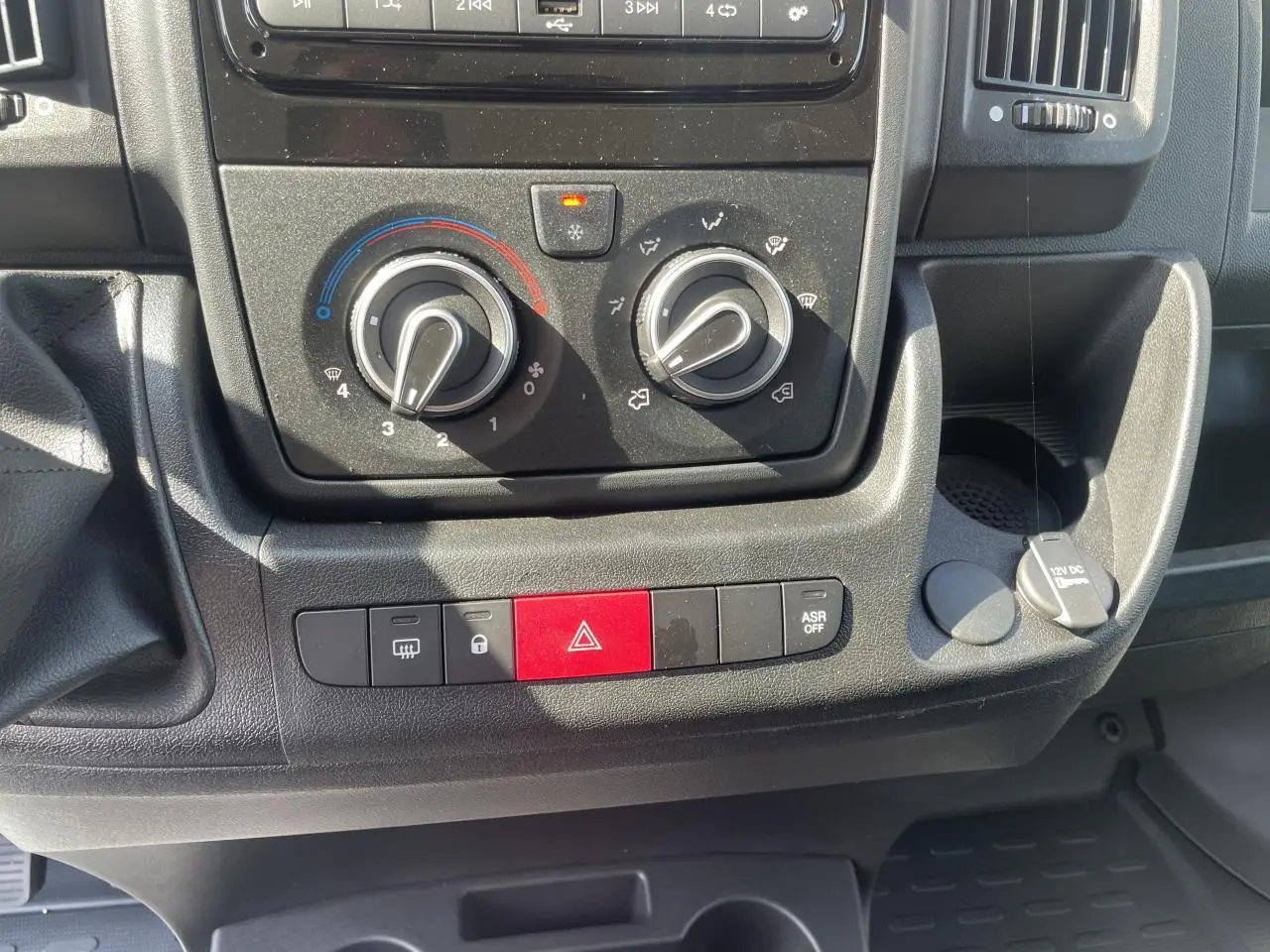 Vue rapprochée du tableau de bord noir du Citroën Jumper 2023, montrant les commandes de climatisation et les boutons de sécurité.