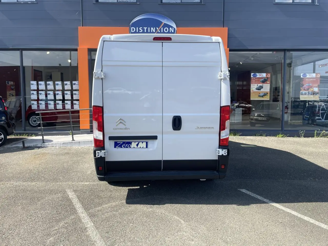 Vue arrière d’un Citroën Jumper blanc 2023 garé devant une vitrine avec portes battantes tôlées et feux rouges verticaux.