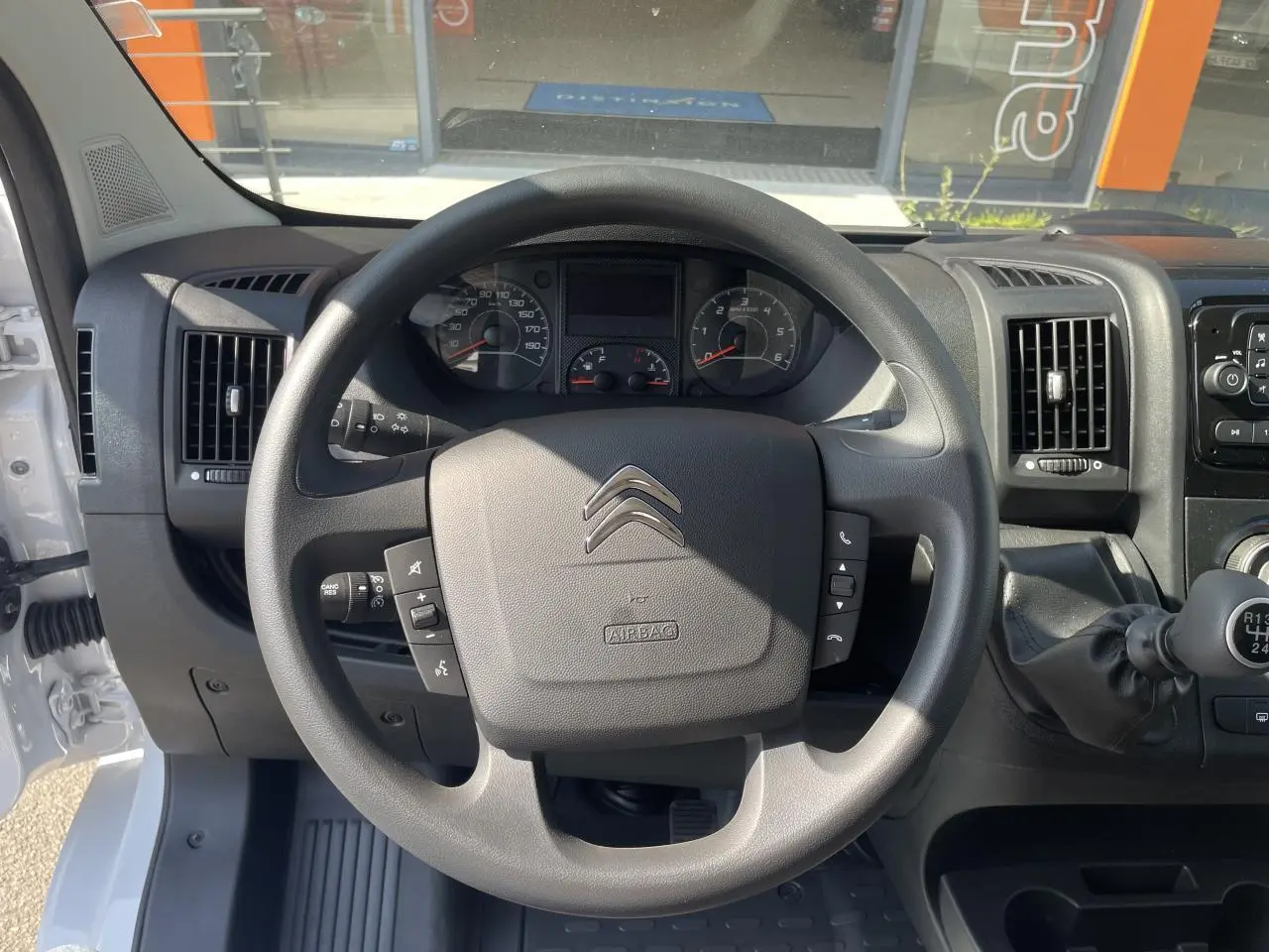 Vue rapprochée du volant et du tableau de bord du Citroën Jumper blanc 2023 avec levier de vitesses manuel et commandes au volant.