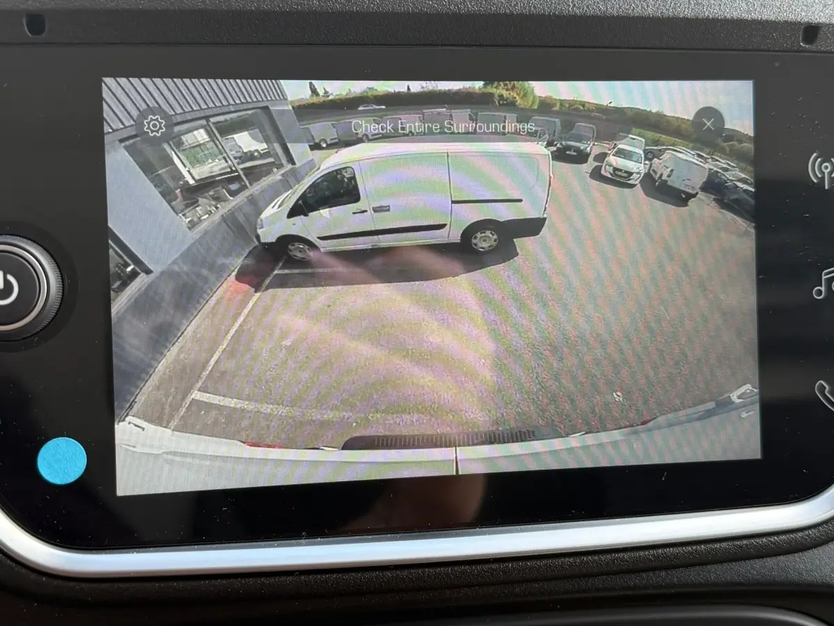 Vue caméra arrière montrant un utilitaire blanc IVECO Daily 35S18 garé de profil côté gauche près d’un bâtiment.