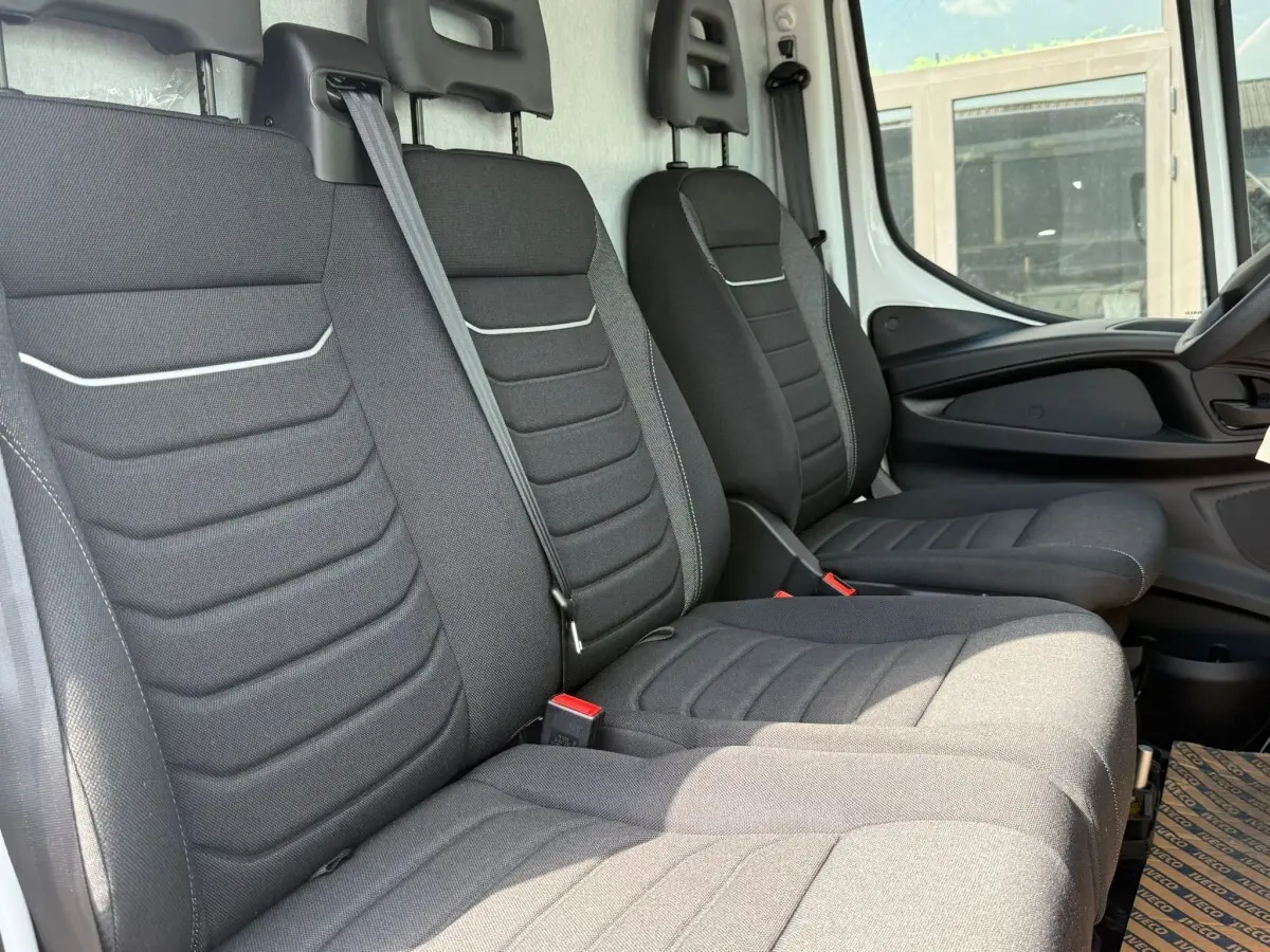 Intérieur du Iveco Daily 35S18 2026, vue latérale des sièges avant noirs avec ceintures de sécurité visibles.