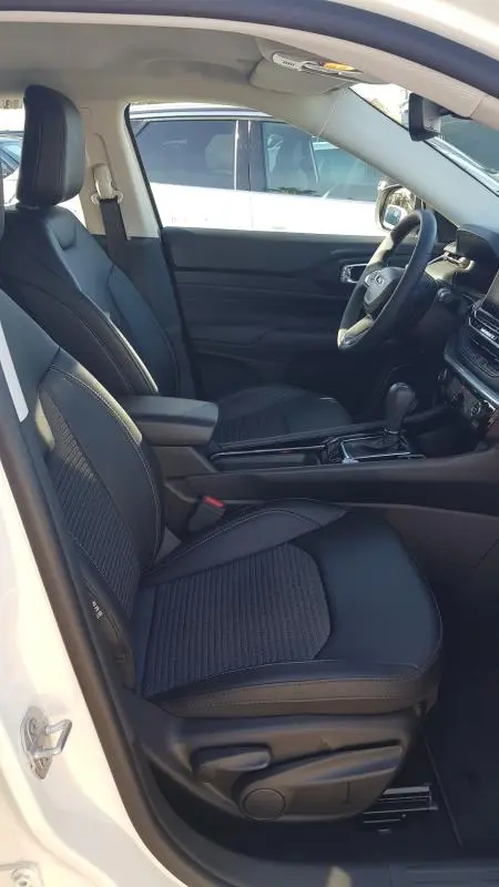 Vue intérieure côté conducteur du Jeep Compass blanc 2024, sièges noirs avec accoudoir central et tableau de bord moderne.