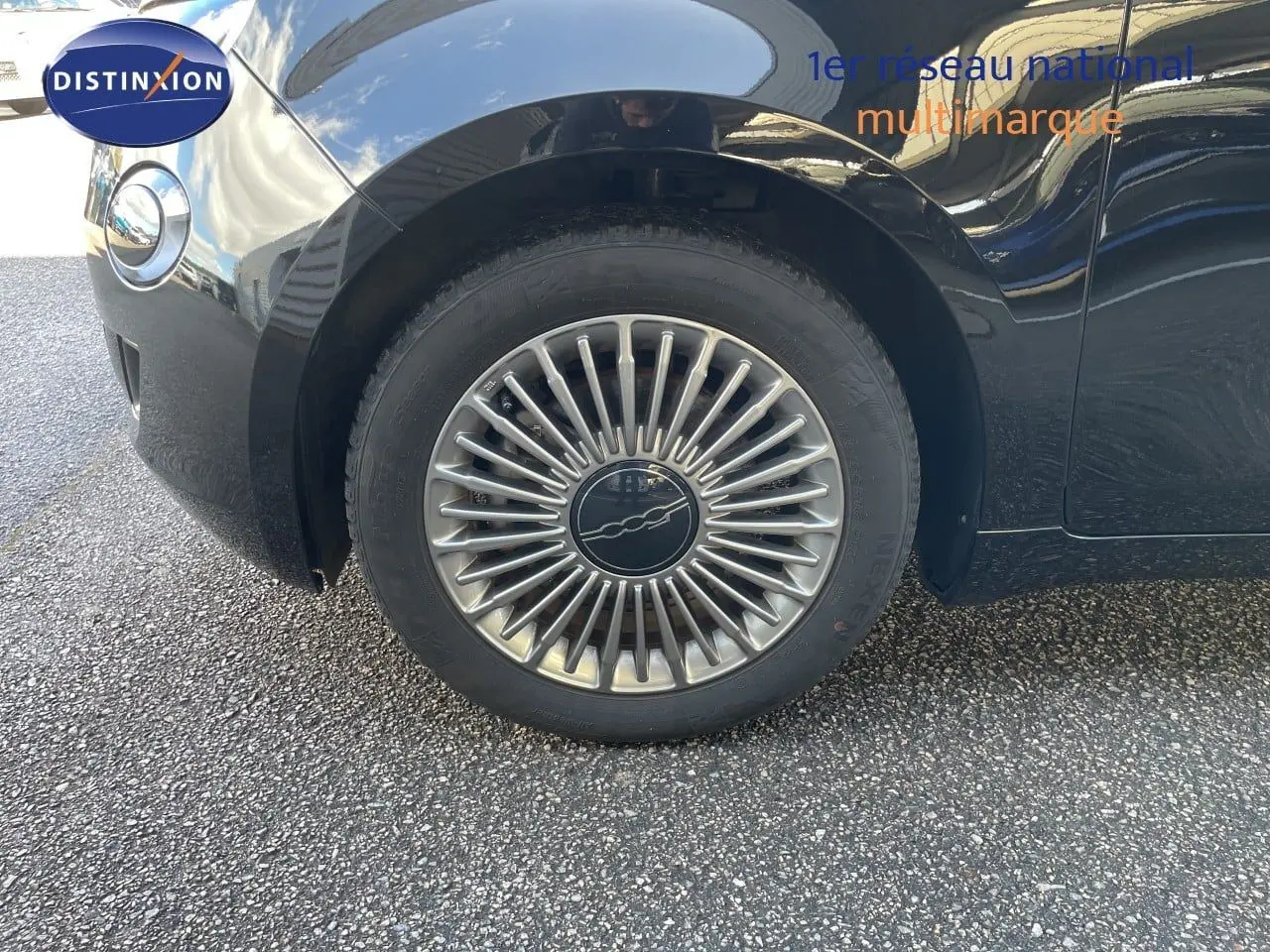 Gros plan sur la roue avant gauche d'une FIAT 500 électrique noir onyx, mettant en valeur la jante design étoilée.