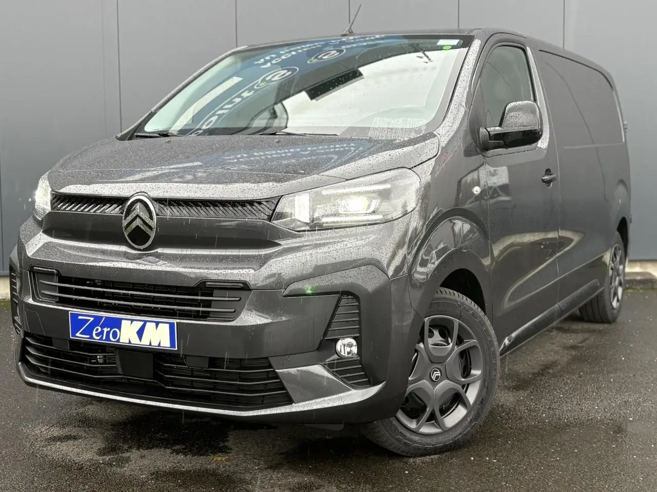 Citroën Jumpy gris titane en 3/4 avant droit sous la pluie avec phares Full LED allumés et jantes noires.