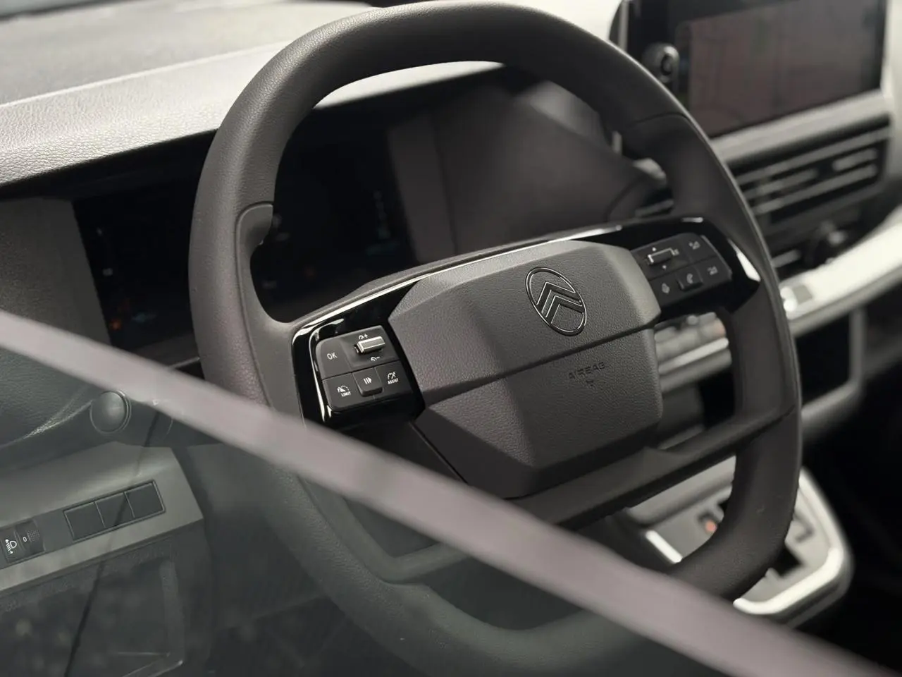 Gros plan sur le volant noir du Citroën Jumpy 2025, avec commandes intégrées et tableau de bord numérique en arrière-plan.