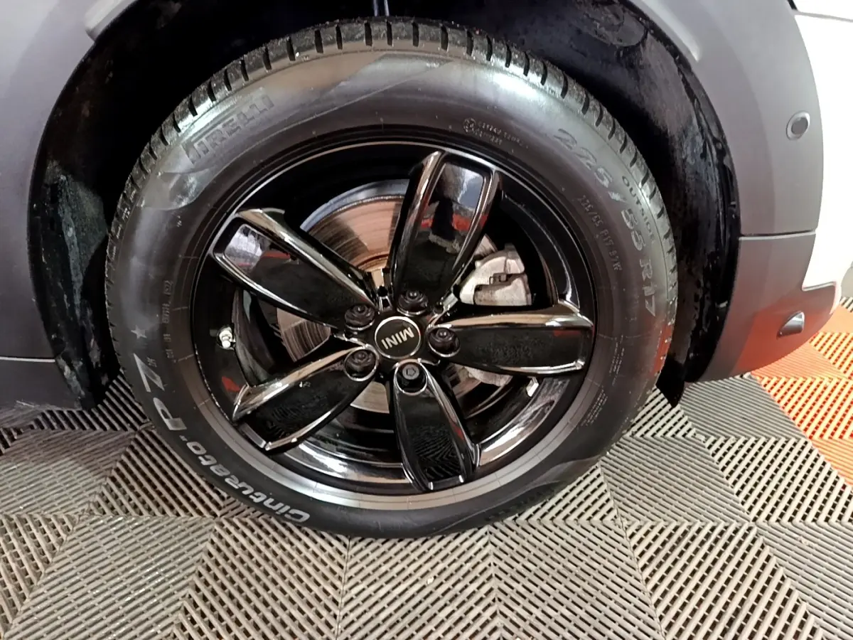 Gros plan sur la roue avant droite d'une MINI Countryman gris clair avec jante noire brillante à cinq branches.