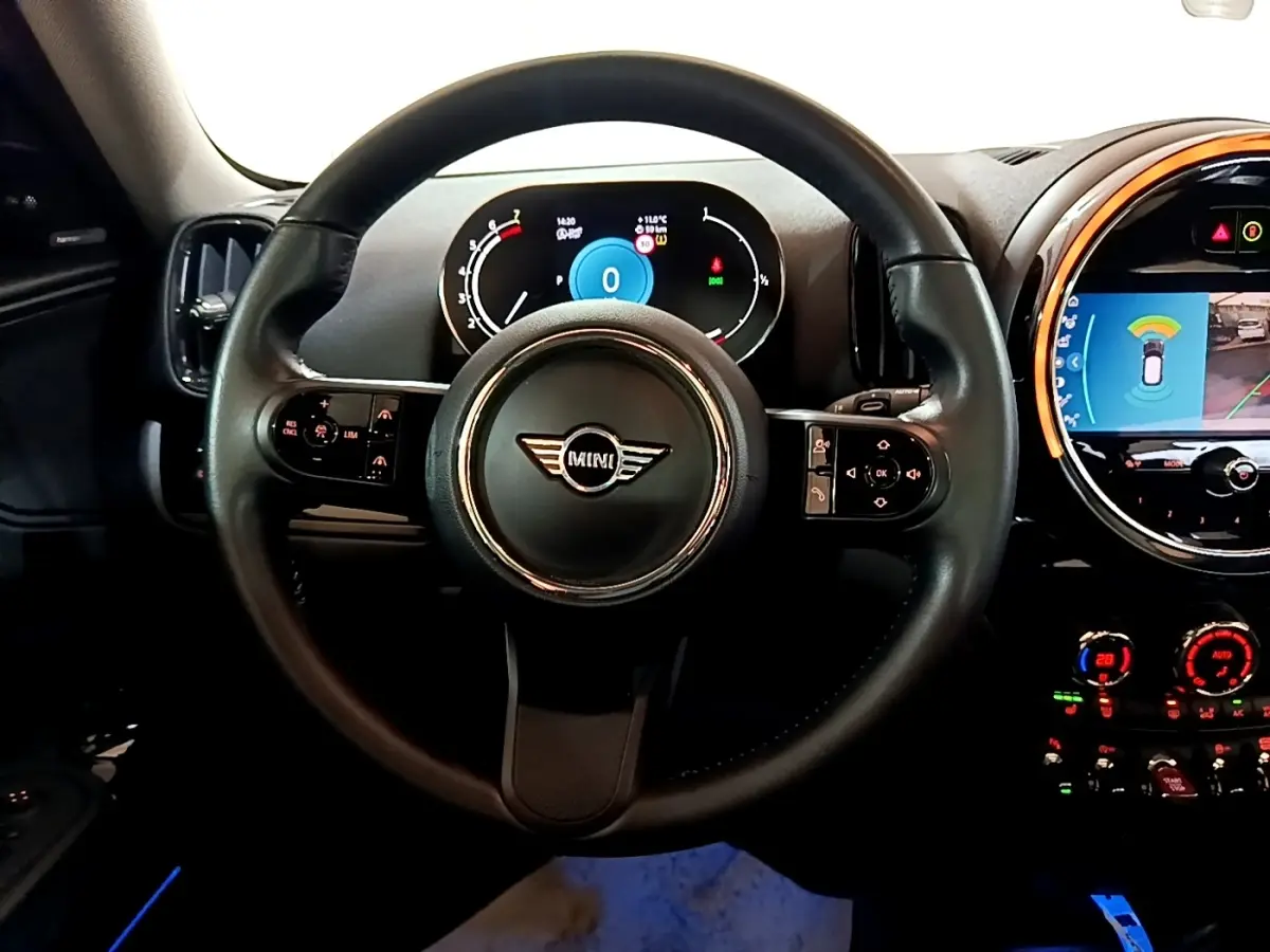 Vue intérieure centrée sur le volant cuir MINI avec tableau de bord digital et écran tactile central éclairé.