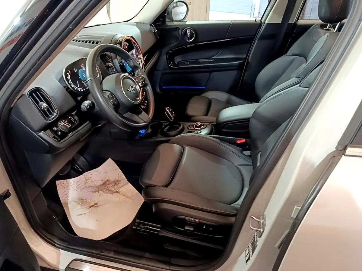 Intérieur côté conducteur du MINI Countryman gris clair 2022, sièges cuir noirs et tableau de bord avec éclairage bleu.